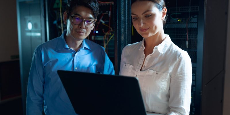 Zwei IT-Fachkräfte arbeiten gemeinsam an einem Laptop – digitale Zusammenarbeit und moderne Technologien im öffentlichen Sektor.